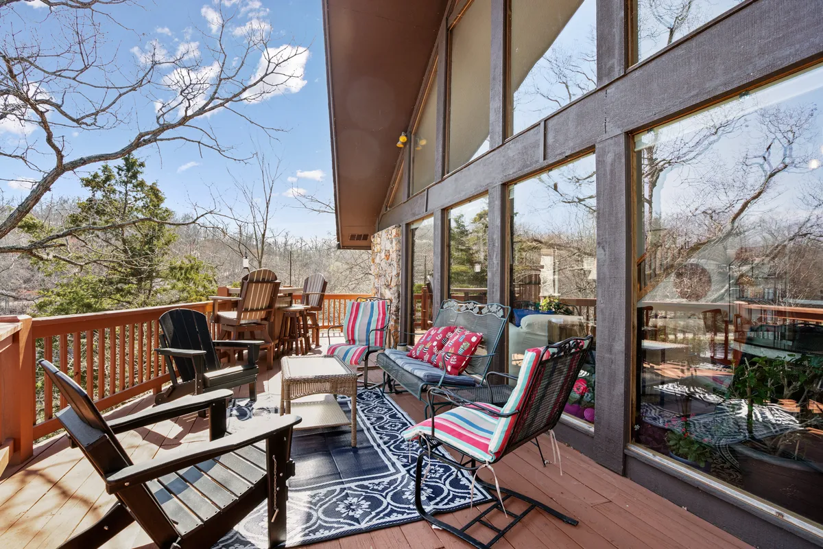A spacious deck with comfortable seating and decorative pillows, bordered by a wooden railing. Large windows hint at expansive water views beyond, and the tranquil mood is enhanced by the warm, welcoming outdoor setting. The deck overlooks the lake, providing the perfect vantage point for events or relaxing moments.