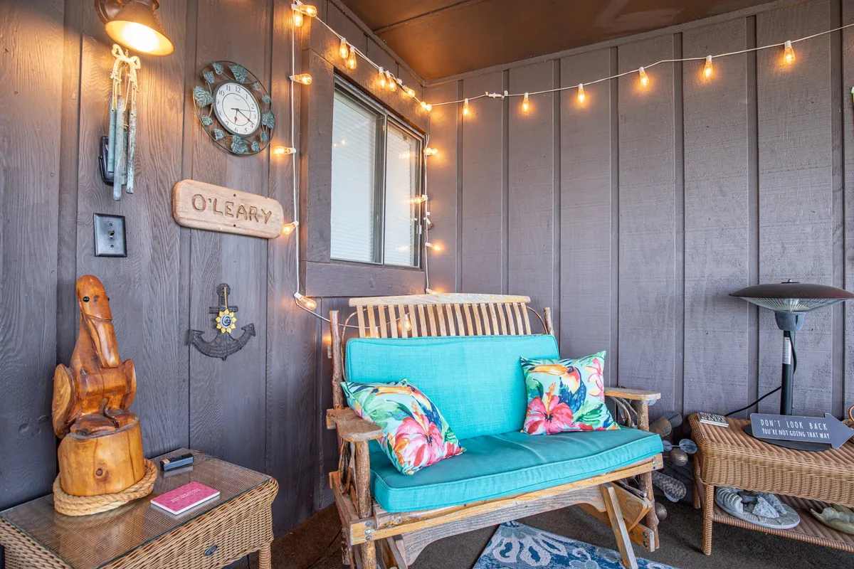 A cheerful, relaxed interior patio space with a wooden bench, string lights, colorful cushions, and decorative accents, creating an inviting setting for evening socializing or quiet moments with loved ones.