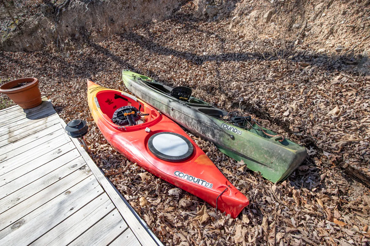 Close-up of a wooden deck with vibrant red and green kayaks ready for use. The area is surrounded by potted plants, inviting the viewer to imagine launching a kayak adventure from the very edge of the property.