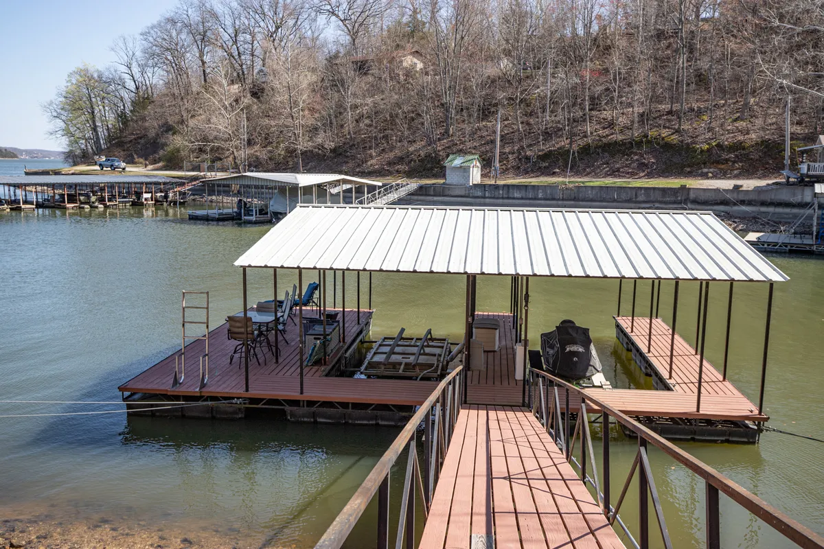A peaceful lakeside dock with boats tied up, ample seating, and shimmering water reflecting the sunset. The dock includes areas for fishing, sunbathing, and relaxing, all set within a tranquil cove.