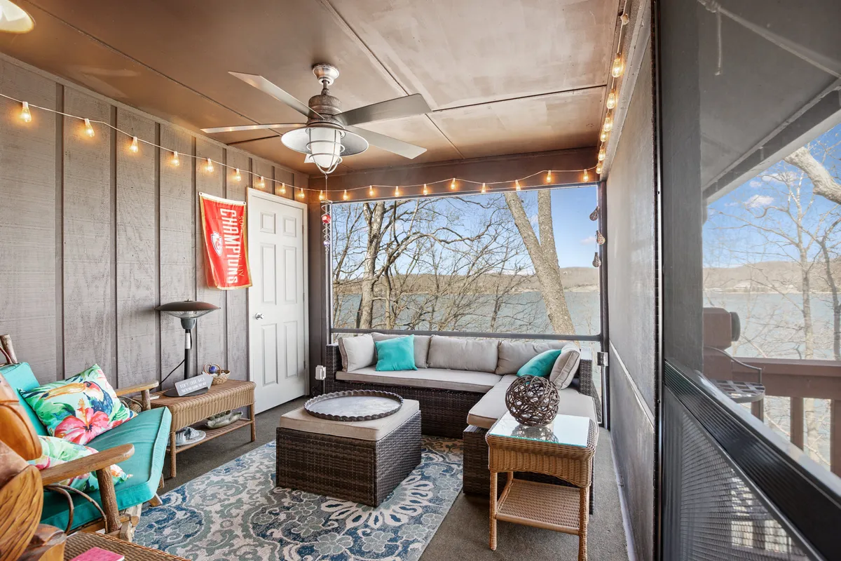 A serene seating area with a comfortable arrangement, decorative rug, large windows revealing lake views, and string lights overhead. The space invites relaxation and socializing while being visually connected to the outdoors.
