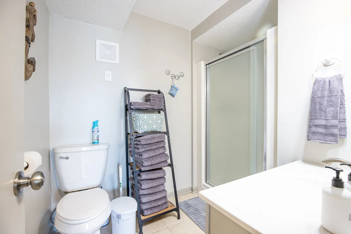 This image depicts a modern, inviting bathroom with a glass shower enclosure, a neatly organized towel rack with fresh towels, a toilet, and a sleek sink area. The space is well-lit and thoughtfully arranged, emphasizing cleanliness and comfort.