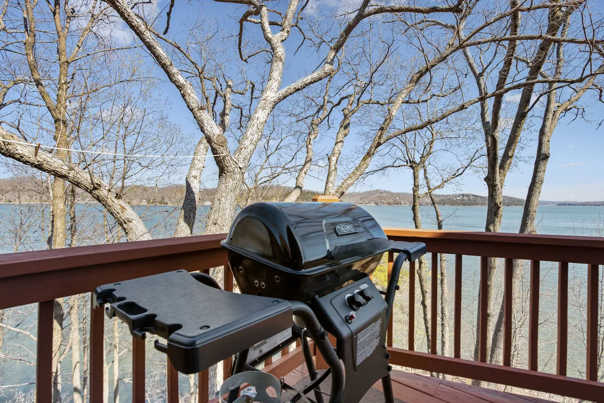 This image features a grill and outdoor seating area with a clear view of the lake and surrounding trees. The setup invites groups to gather for barbecues or casual meals while enjoying the scenic lakeside backdrop.